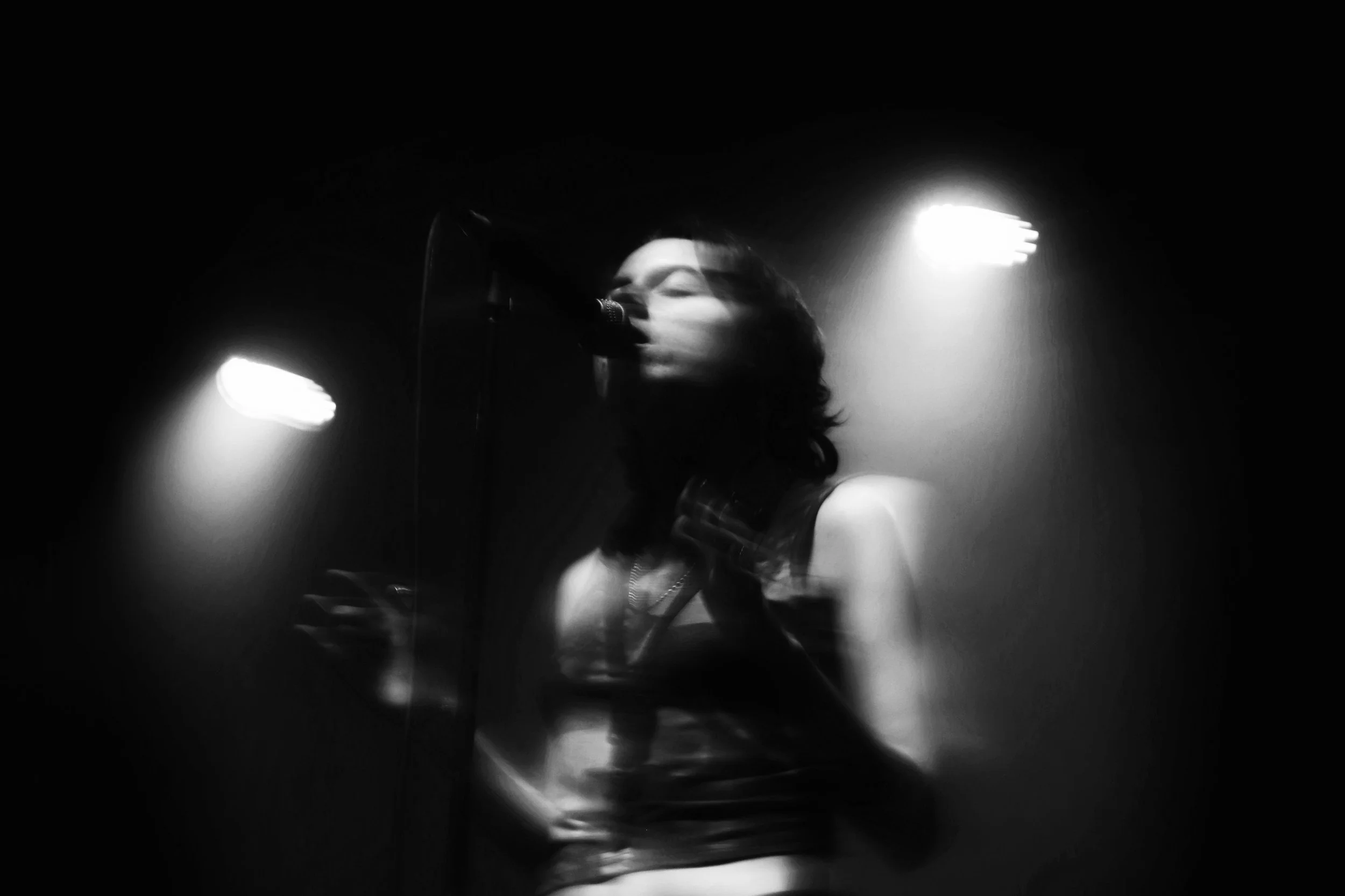 Dark black and white photo of a lone woman singing into a microphone.